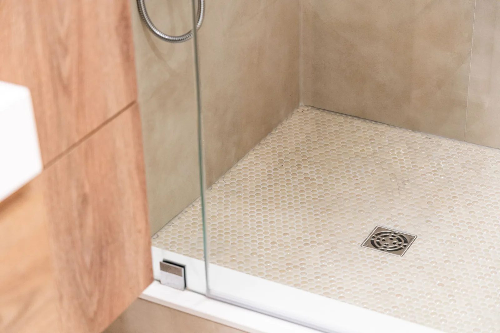 Walk-in shower clad in wood-look tile with a mosaic-tiled floor behind a frameless glass panel.
