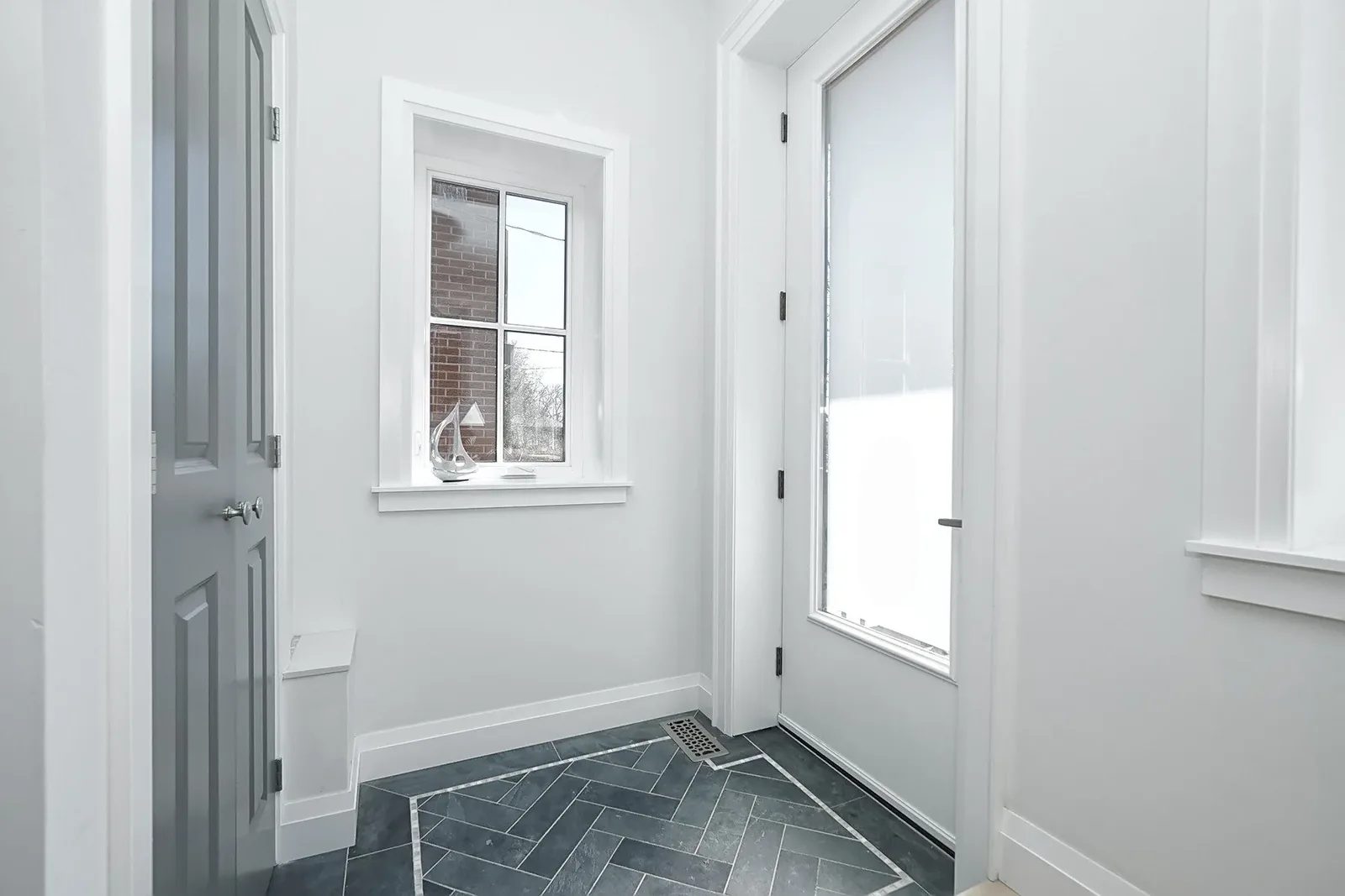 Bright white entry with charcoal herringbone tile, grey interior door, glass front door and trim.