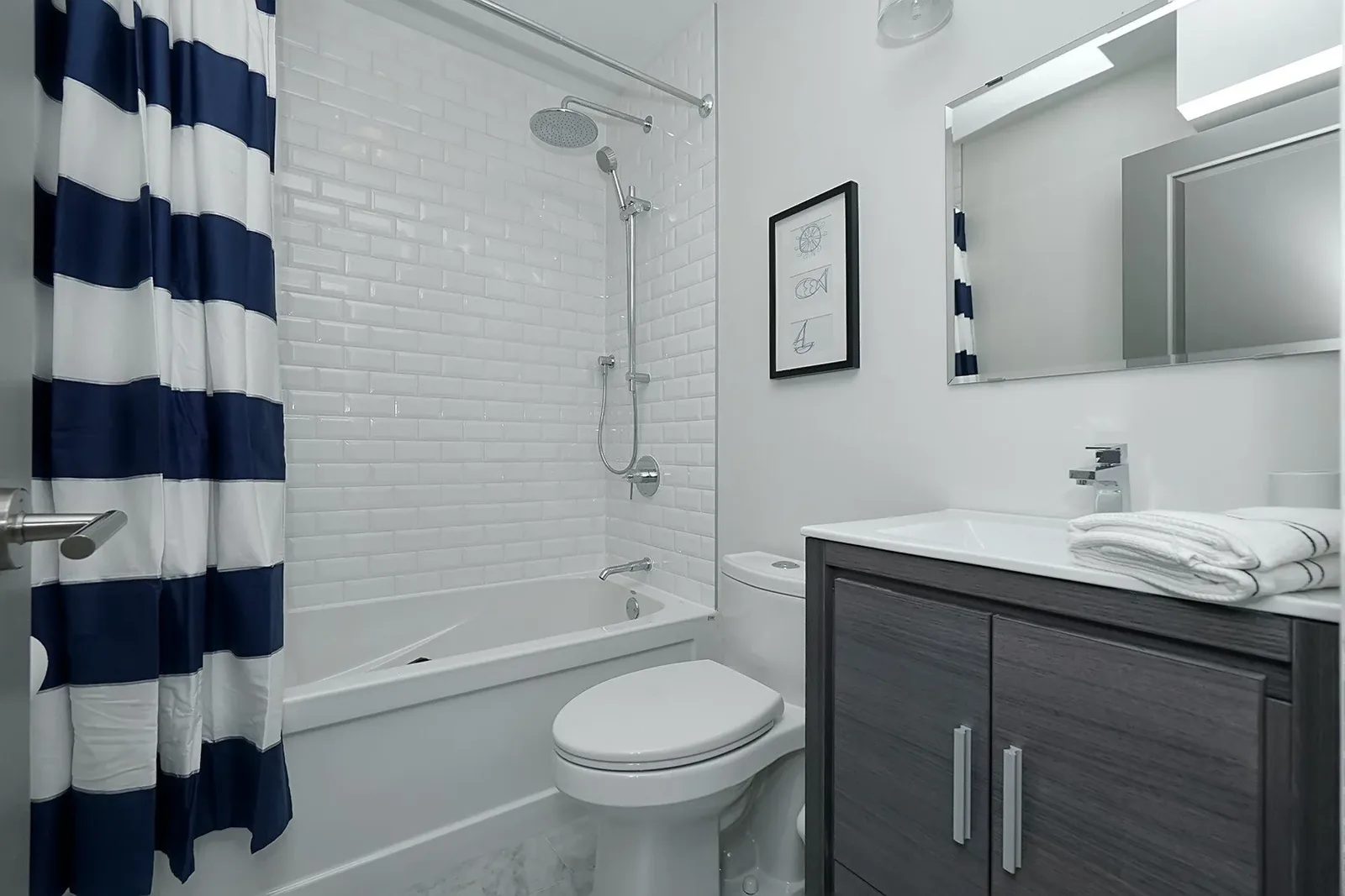 Compact bathroom with white subway tile, navy striped curtain, chrome fixtures and a charcoal vanity.