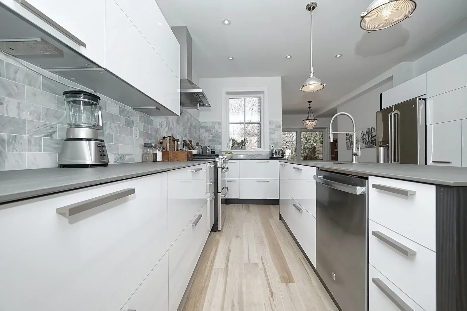 Bright white Toronto kitchen renovation with grey tile backsplash, island, pendants and light oak flooring.