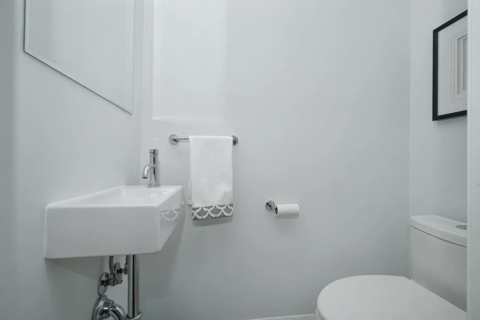 Compact white powder room with a wall mounted sink, chrome fixtures, towel bar, and toilet.