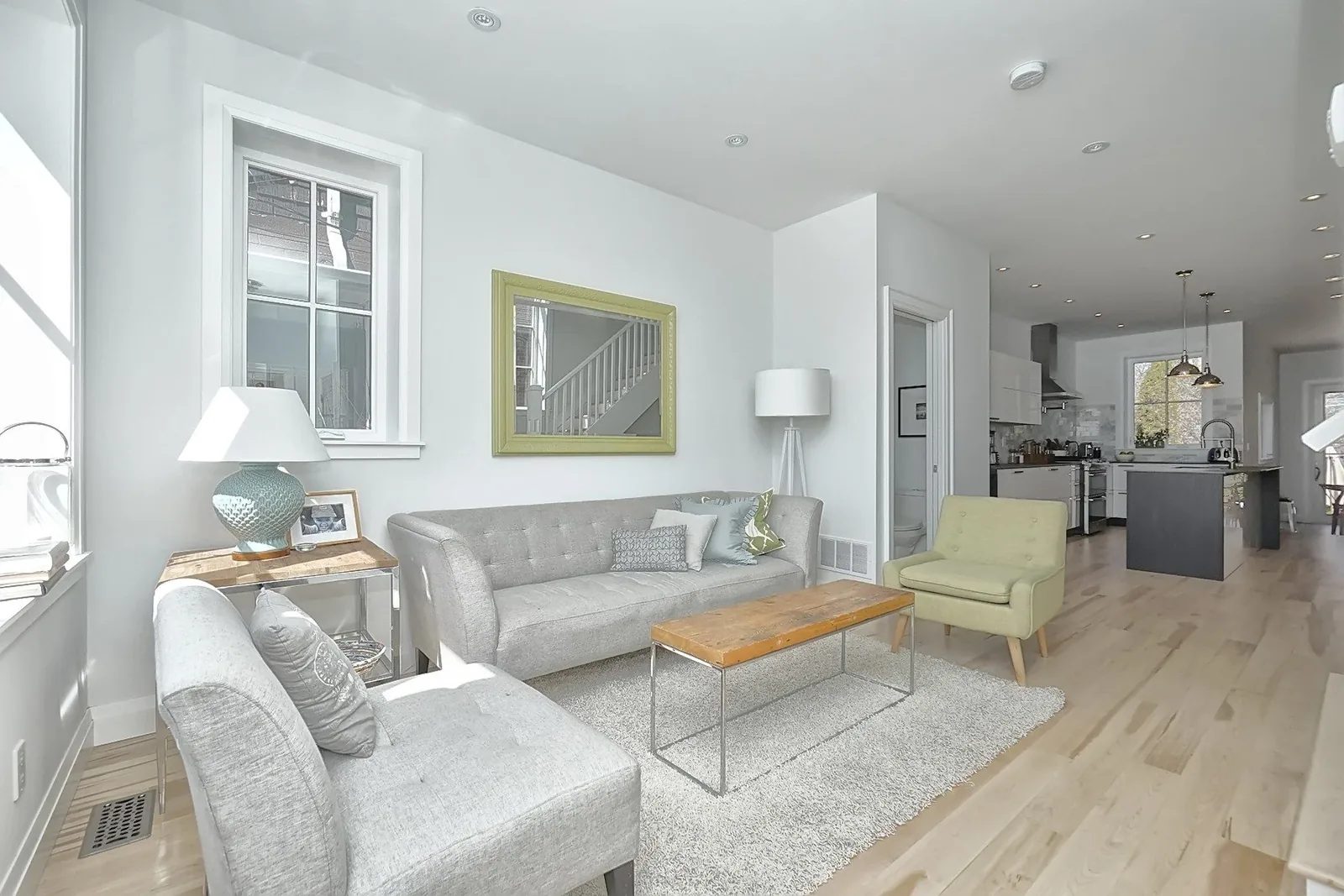 Bright open-concept living room and kitchen with light hardwood floors and soft neutral colour palette.