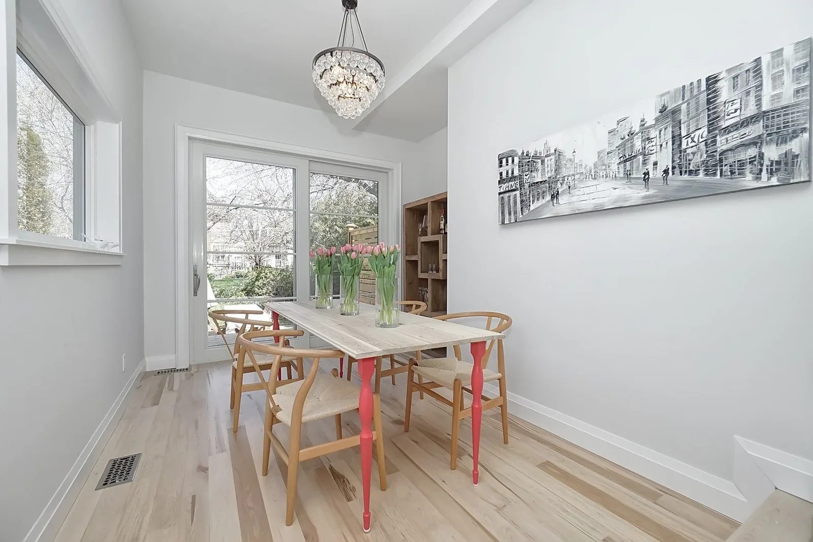 Bright Toronto dining room with warm white walls, pale hardwood flooring, large windows, and a crystal chandelier.