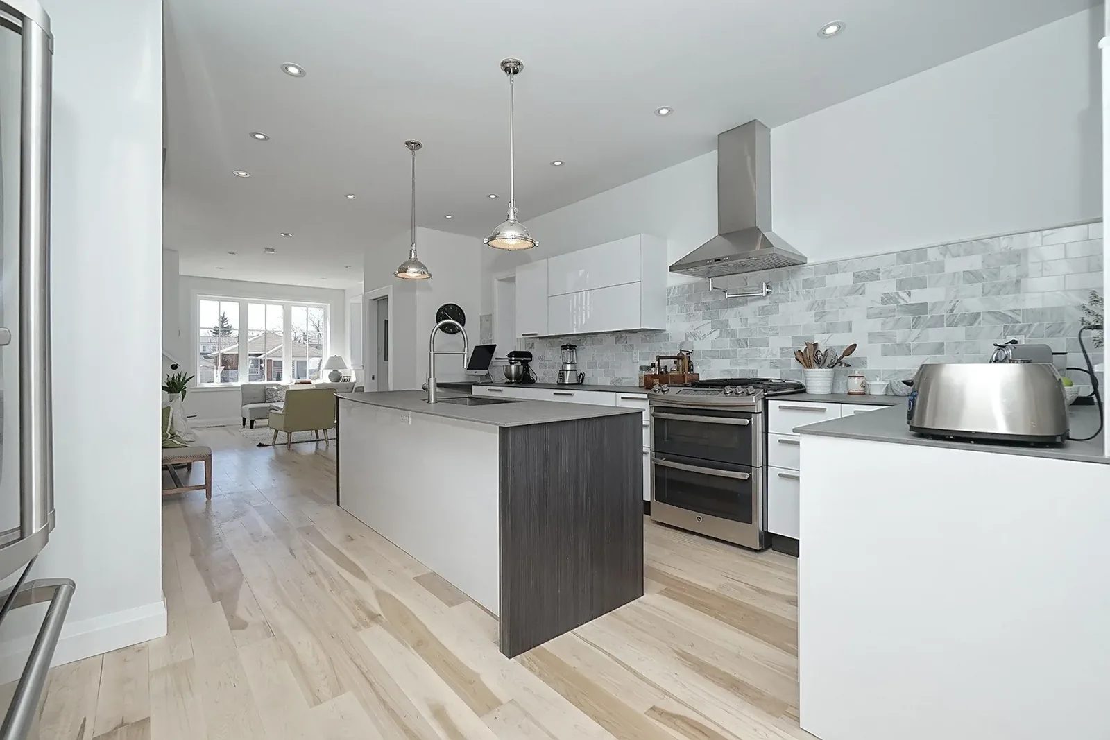 Finished open-concept kitchen with warm white cabinetry, a large island, stone backsplash, and light oak flooring.