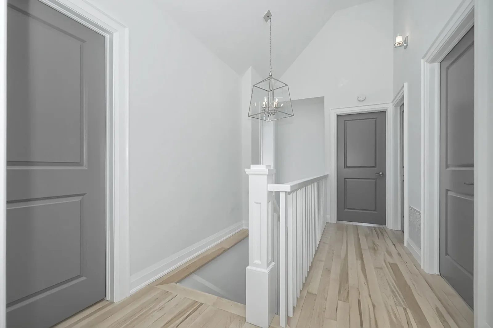 Finished upstairs hallway with grey doors, white trim, light wood flooring, and a glass pendant over the stairs.