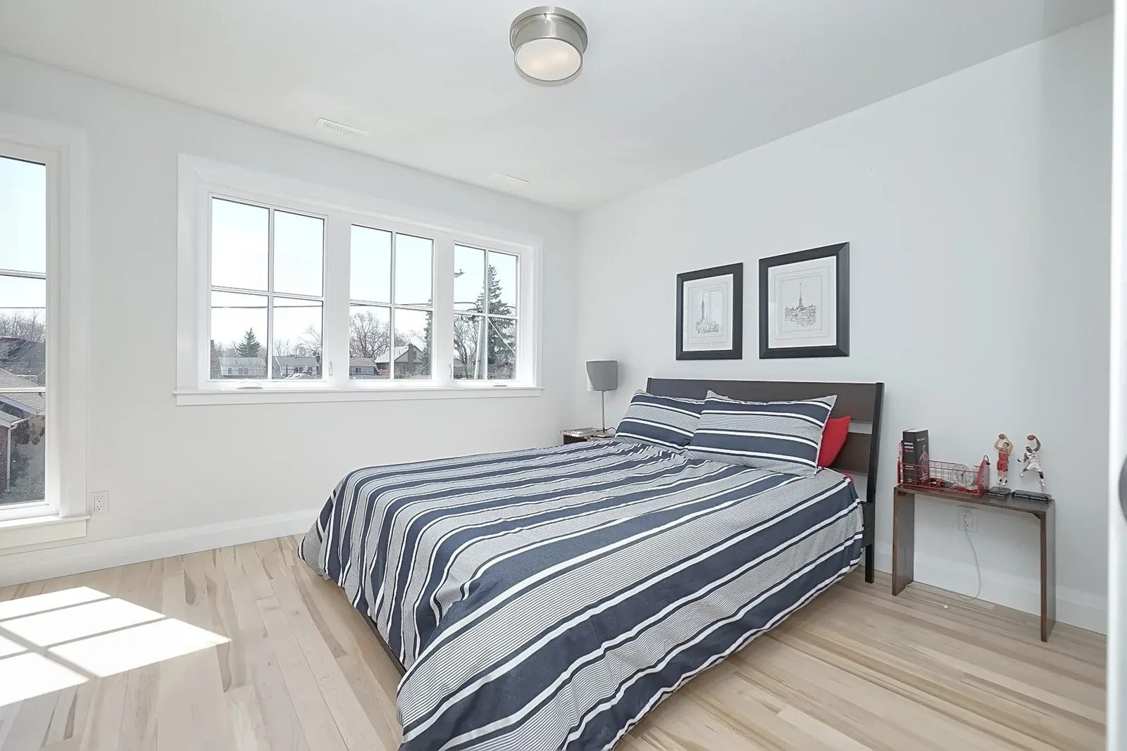 Bright finished bedroom with white walls, pale hardwood floors, large windows, and navy striped bedding.