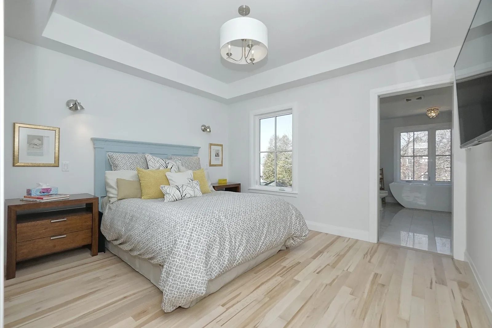 Bright Toronto bedroom with pale wood flooring, tray ceiling, and a clean ensuite view.
