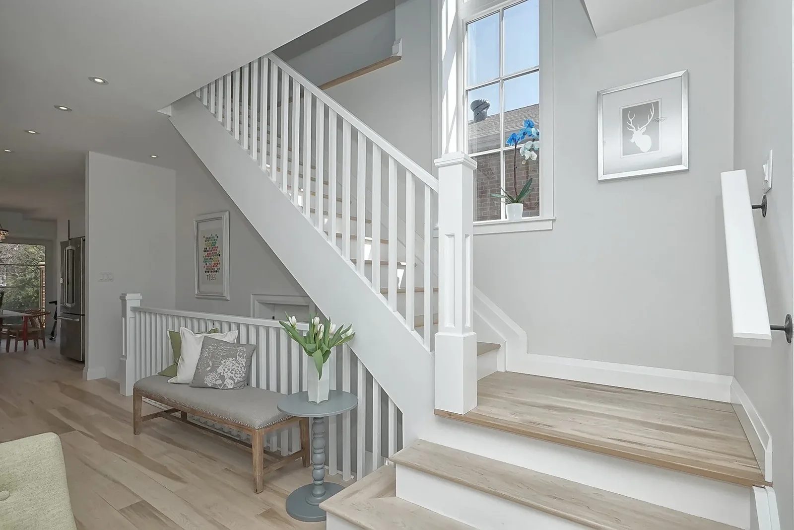 Bright renovated entry with white staircase, pale grey walls, and natural wood flooring.