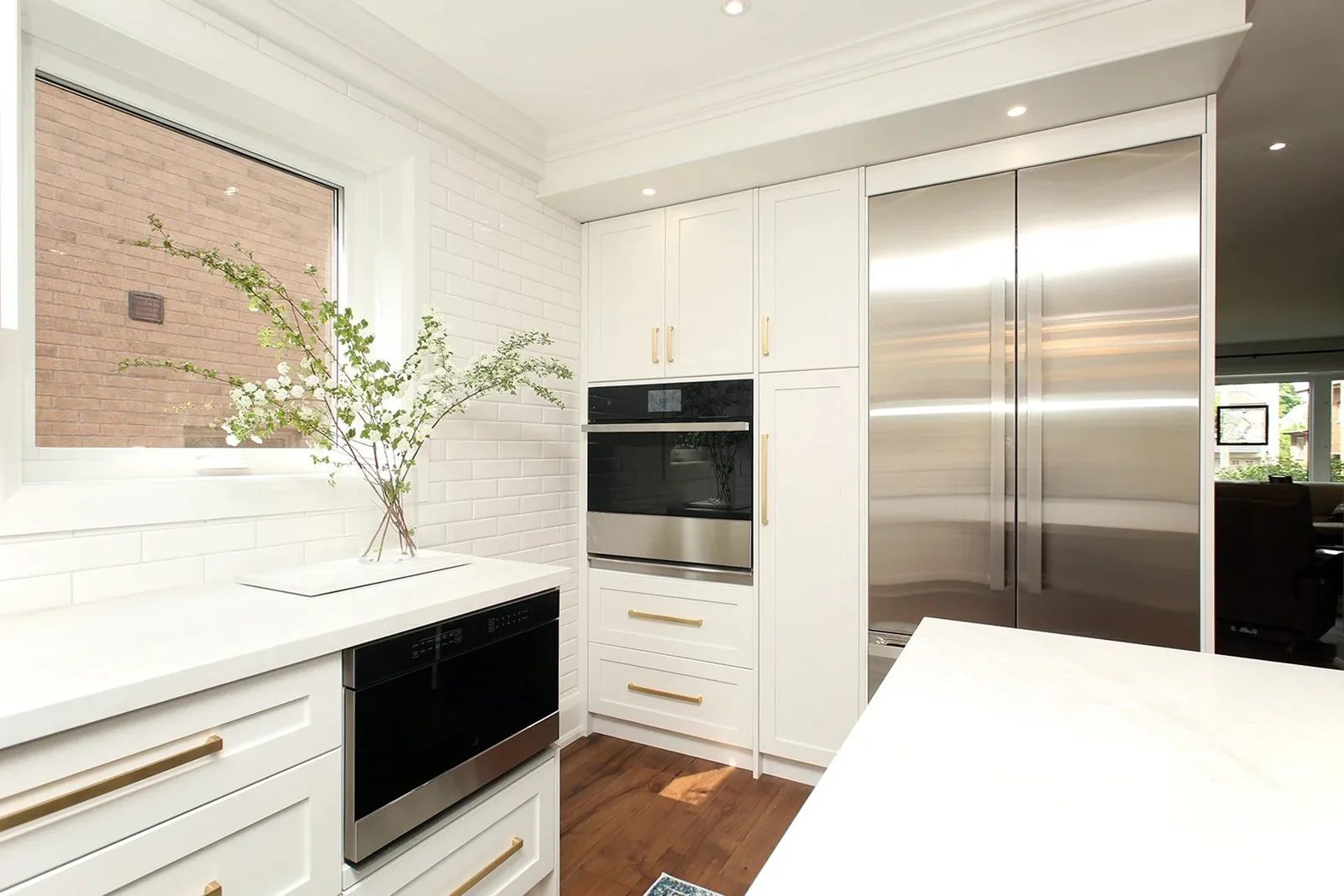 Bright Toronto kitchen showcases white shaker cabinets, brushed brass hardware, and a built in stainless steel refrigerator.