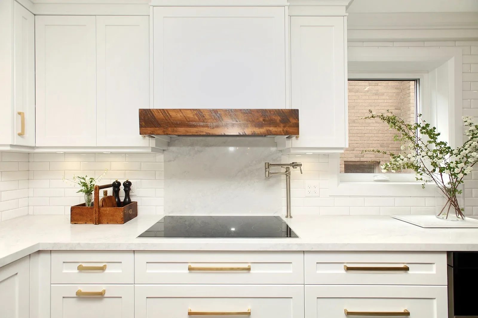 A bright white kitchen with brushed brass hardware and a rustic wood range hood detail.