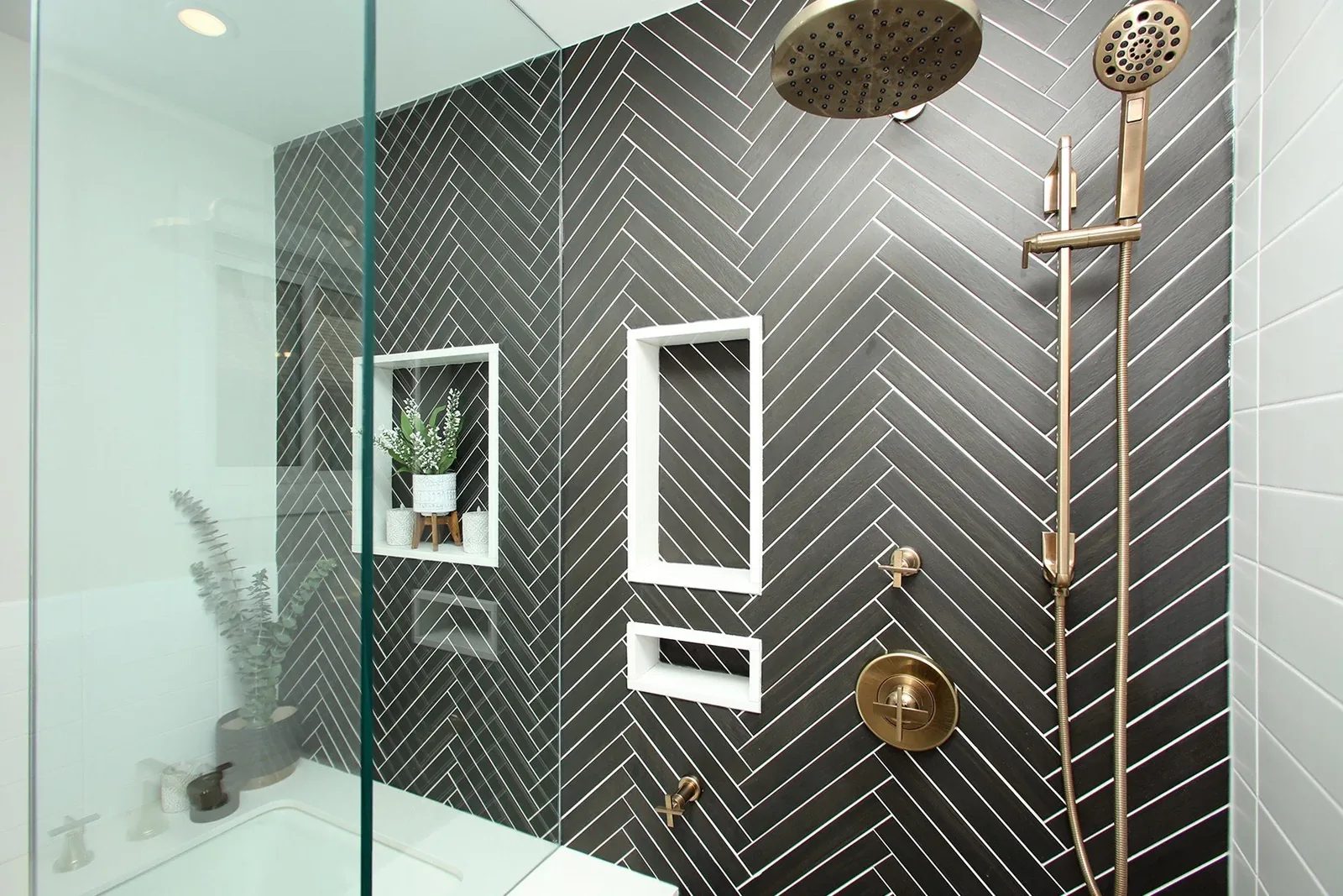 Modern bathroom with charcoal herringbone tile shower and brushed brass fixtures.