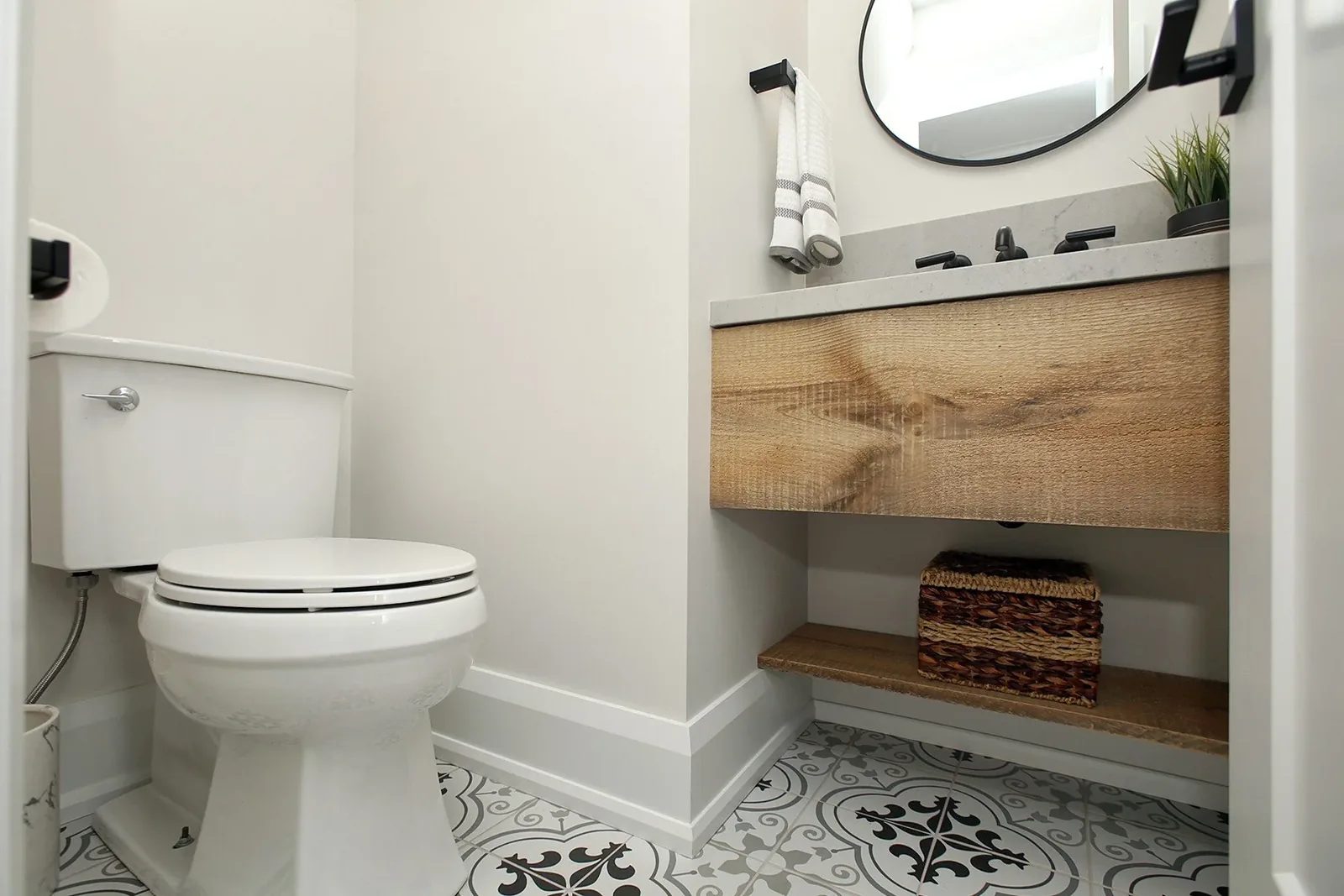 Compact powder room with patterned tile floor, floating wood vanity, and matte black fixtures.