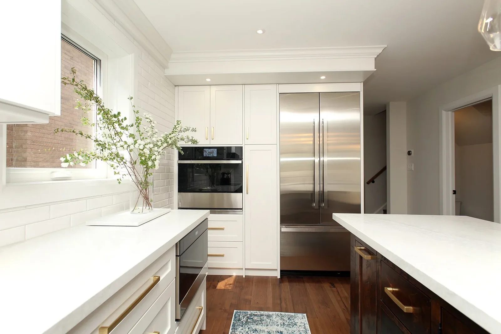 Contemporary Toronto kitchen with warm white cabinets, quartz countertops, a dark wood island, and brushed brass hardware.