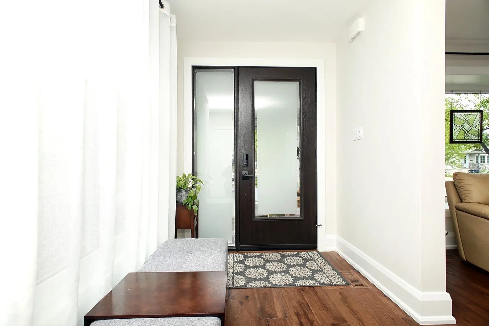 A clean entry features a frosted glass double door, patterned rug, and wood bench.