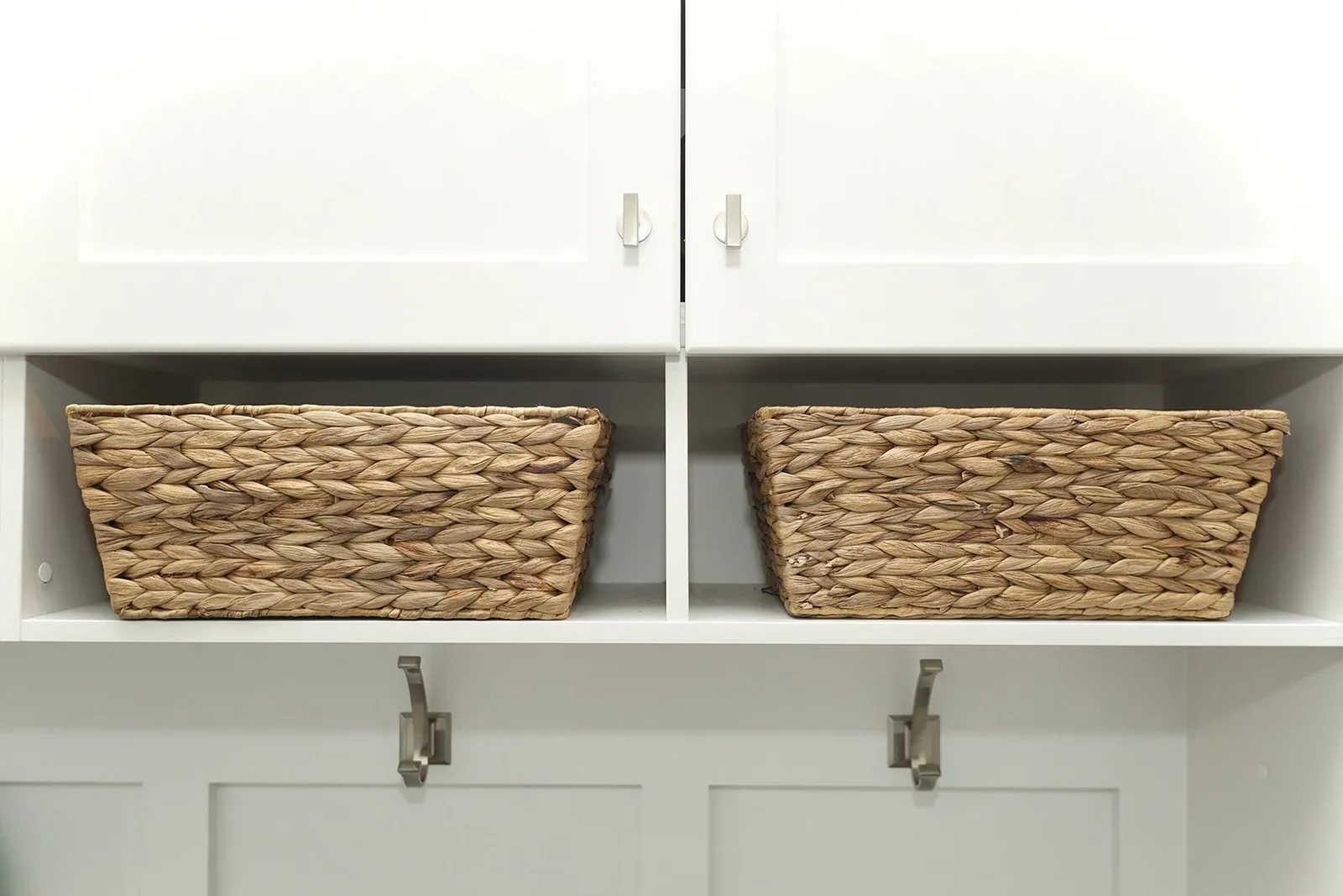 White built-in entry storage with woven baskets, upper cabinets, and brushed metal hooks.
