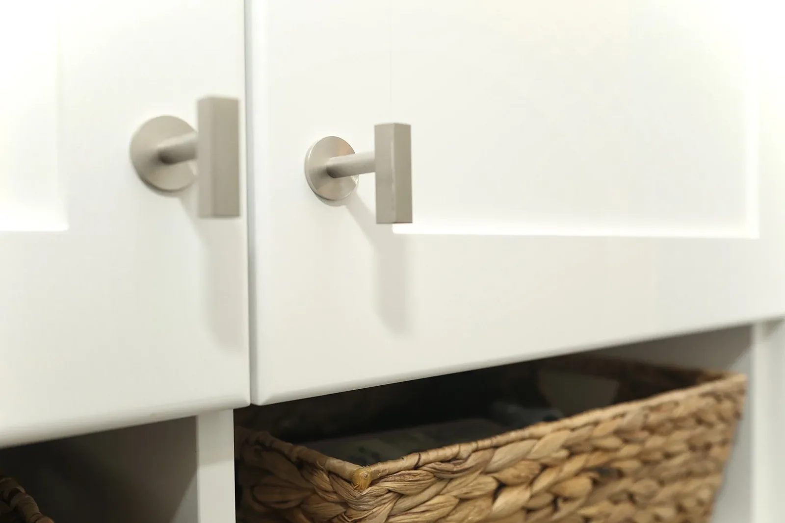 Warm white entry cabinetry with brushed nickel pulls and woven basket storage in a clean, organised detail.