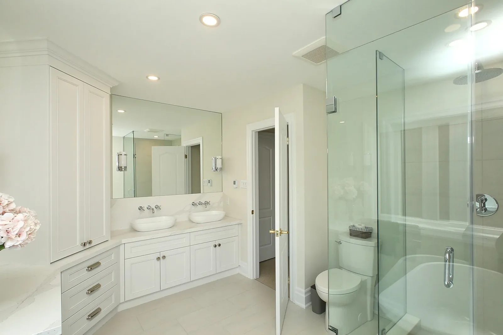 Bright finished bathroom with double vanity, vessel sinks, and a glass enclosed tub and shower.