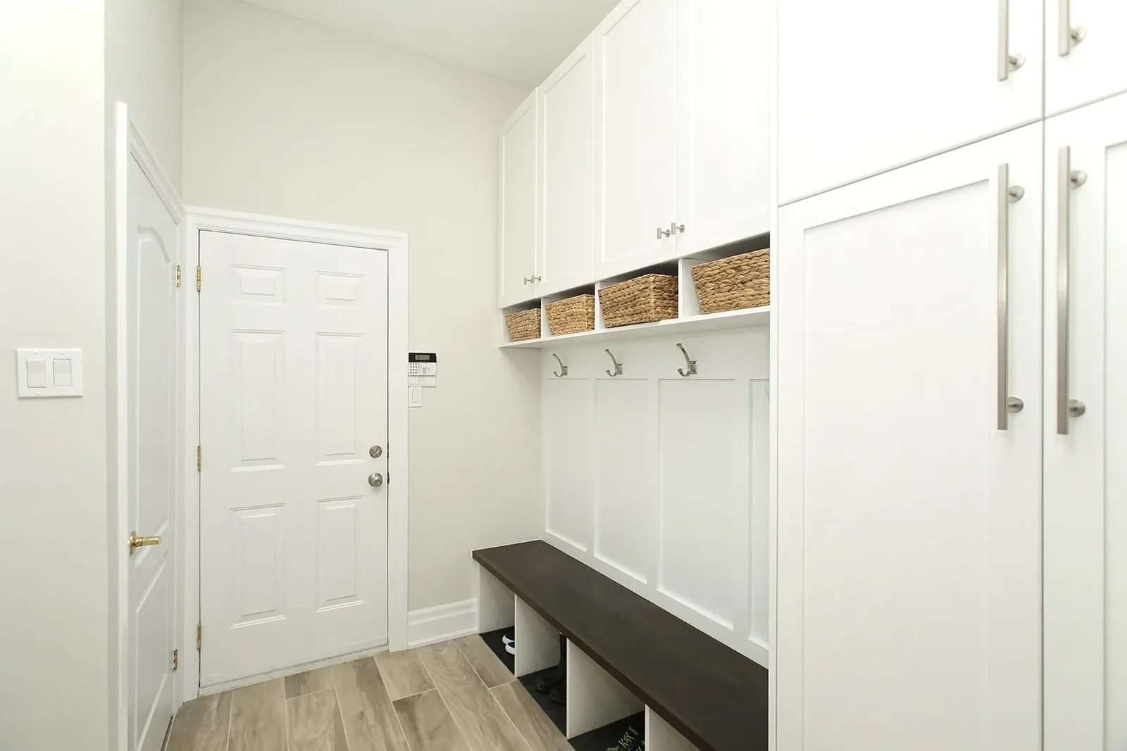 Bright organised entry with white built in storage, hooks, woven baskets and a charcoal bench by the front door.