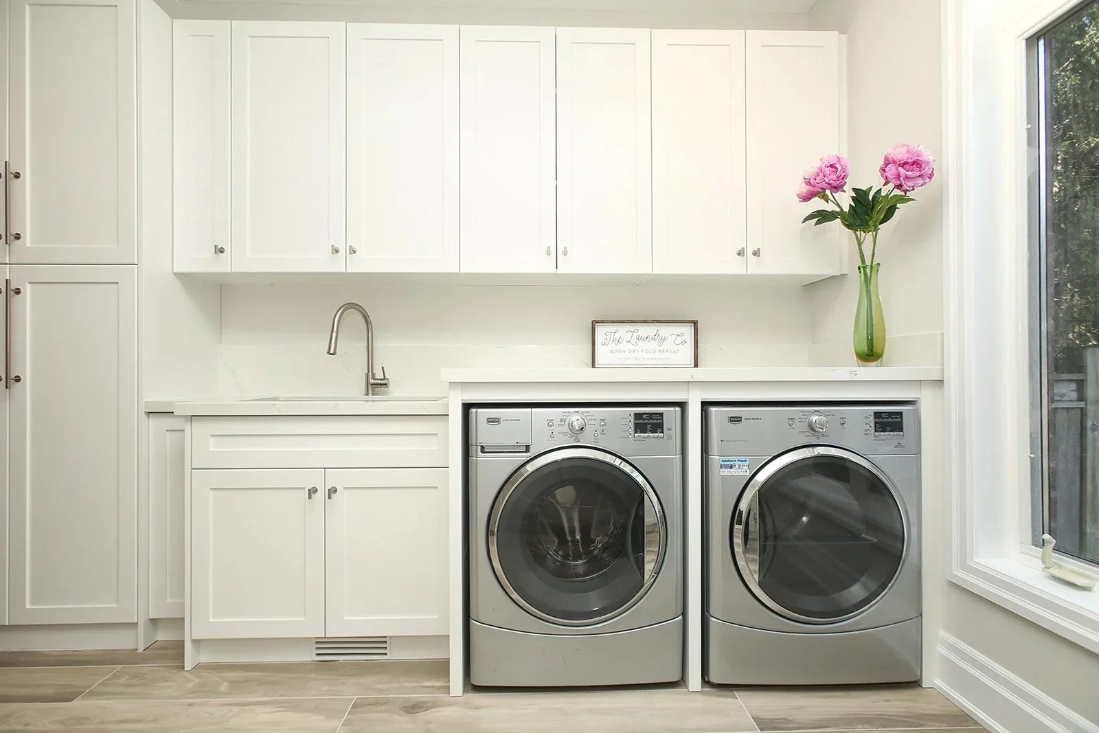 Bright laundry room with white shaker cabinets, a sink, and side by side front load machines.