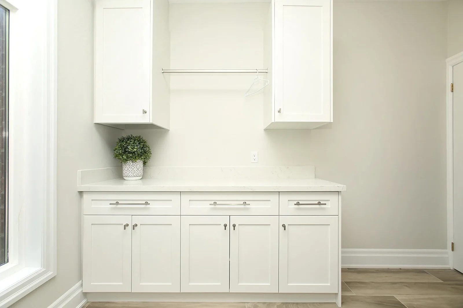 Bright laundry room with white shaker cabinets, quartz counter, hanging rod, and light grey walls.