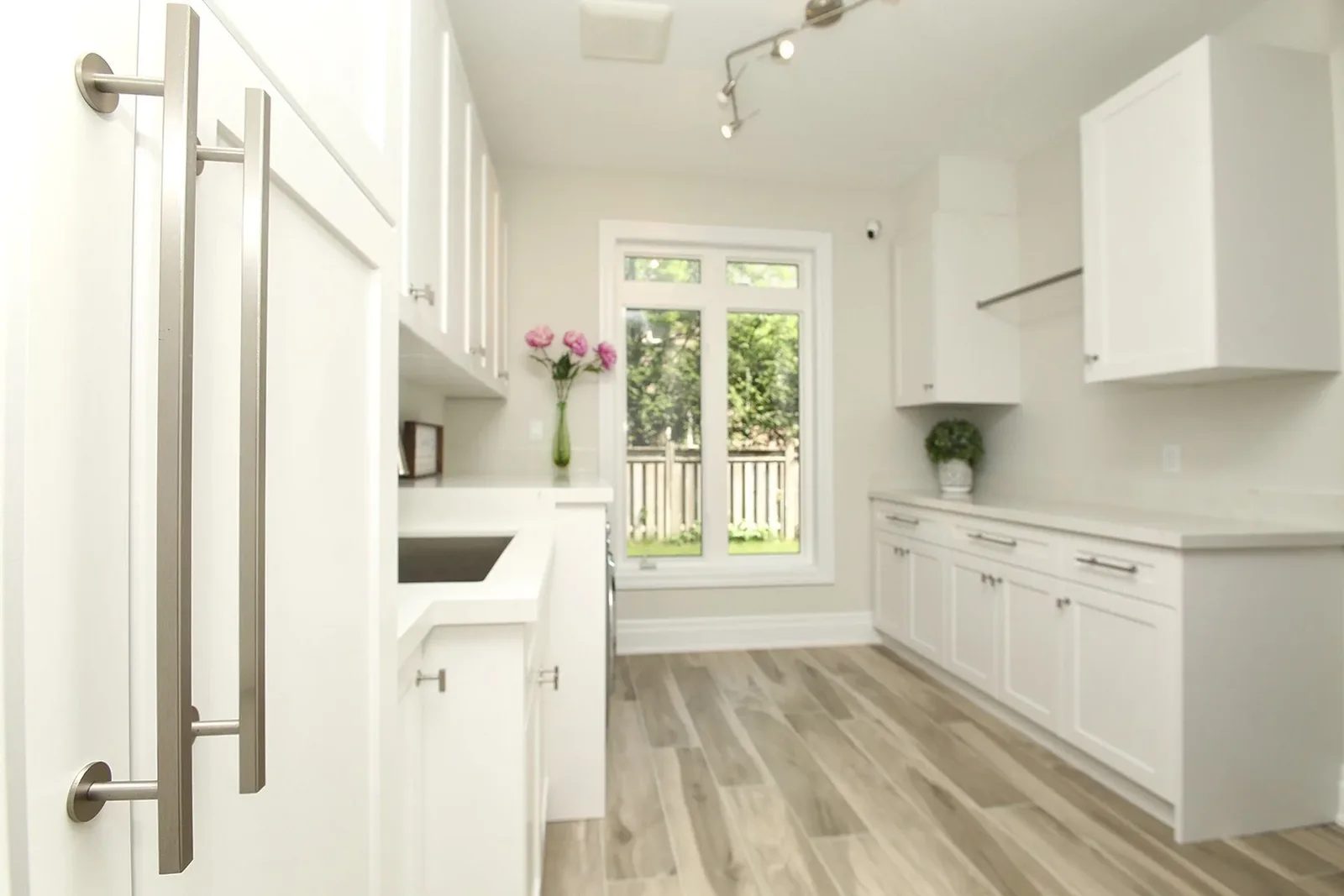 Bright white laundry room with shaker cabinets, quartz counters, a sink, and a large rear window.