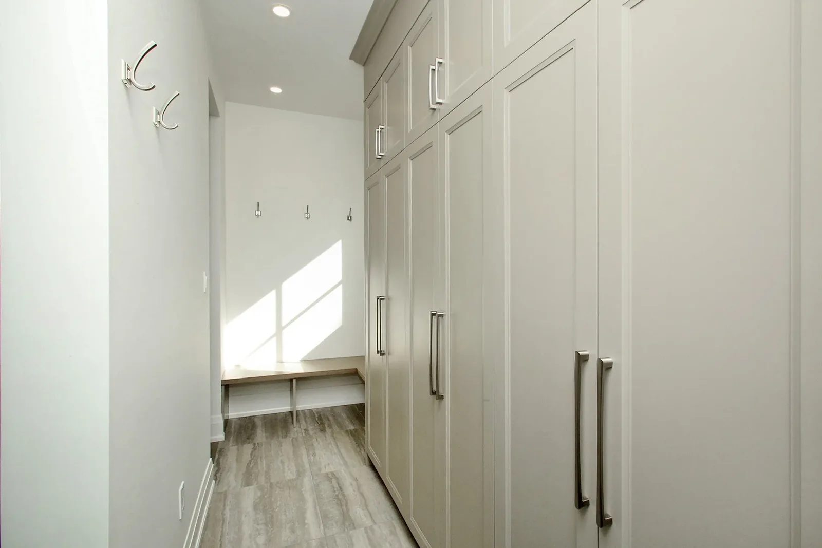 Mudroom with warm grey floor to ceiling cabinets, chrome bar pulls, coat hooks, and a built in oak bench.