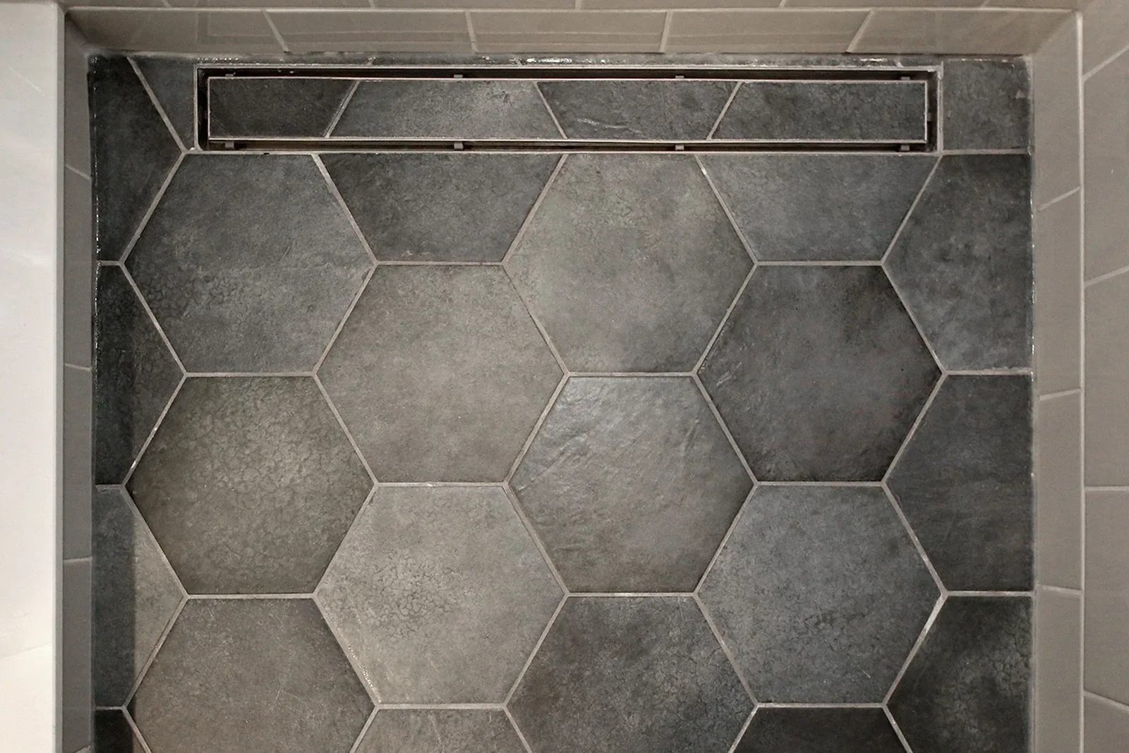 Overhead view of charcoal hexagonal porcelain shower floor tile with stainless steel linear drain channel.