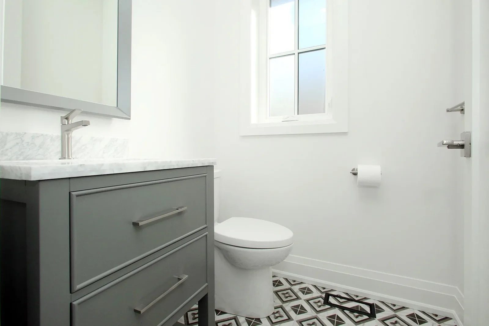 Powder room with grey single vanity, Carrara marble top, and patterned black-and-white encaustic-look floor tile.