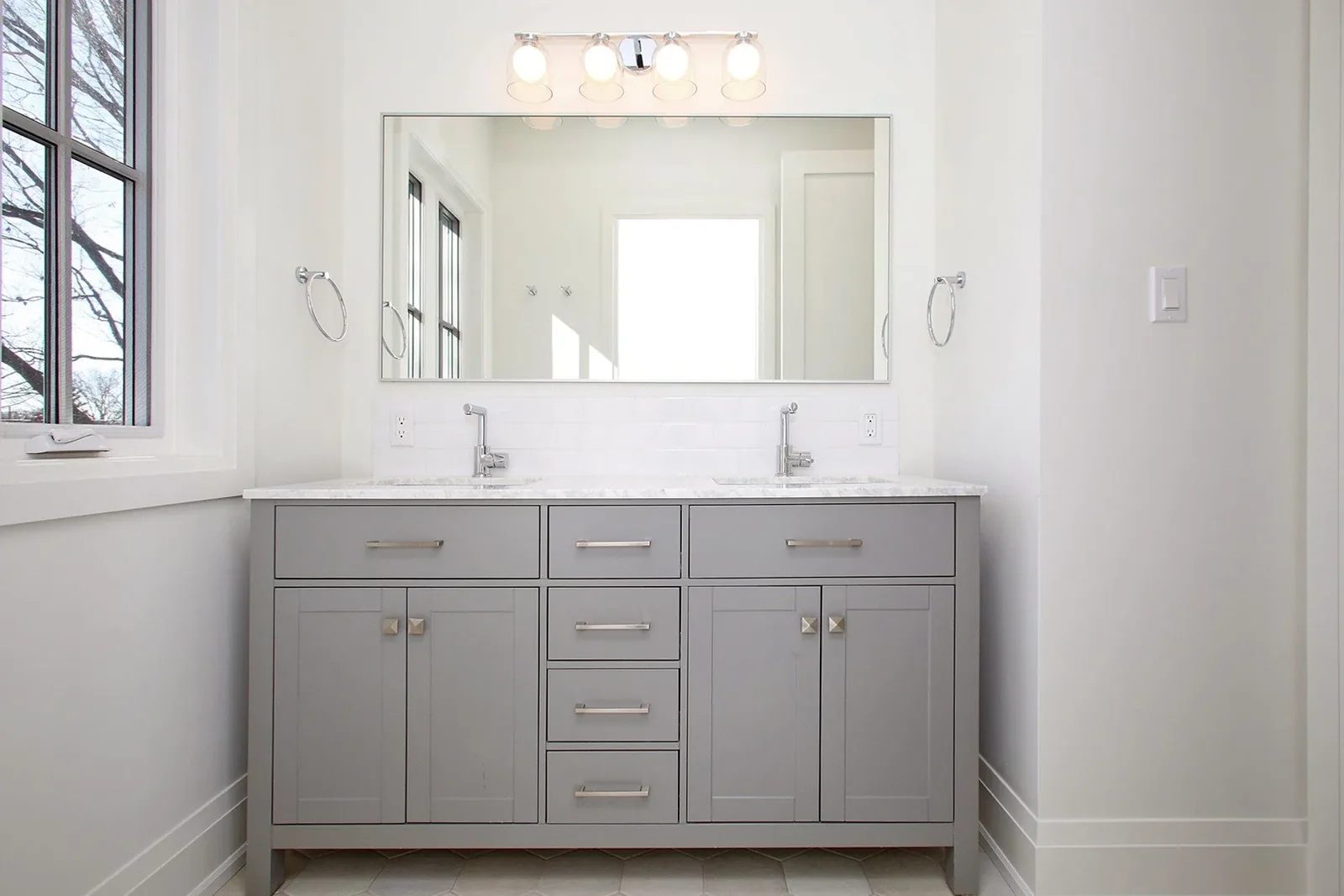 Main bath double-sink grey vanity with Carrara marble top, framed mirror, and four-bulb chrome vanity light.