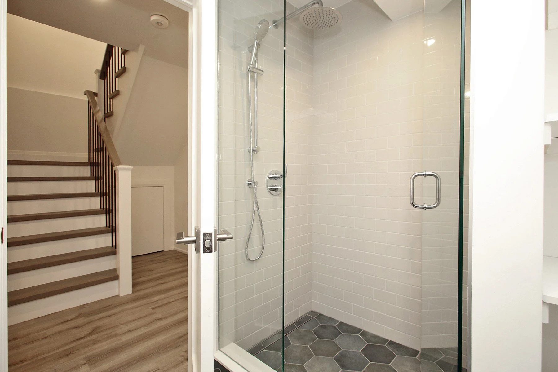 Glass-enclosed walk-in shower with white subway tile, charcoal hex floor, and rain shower head.