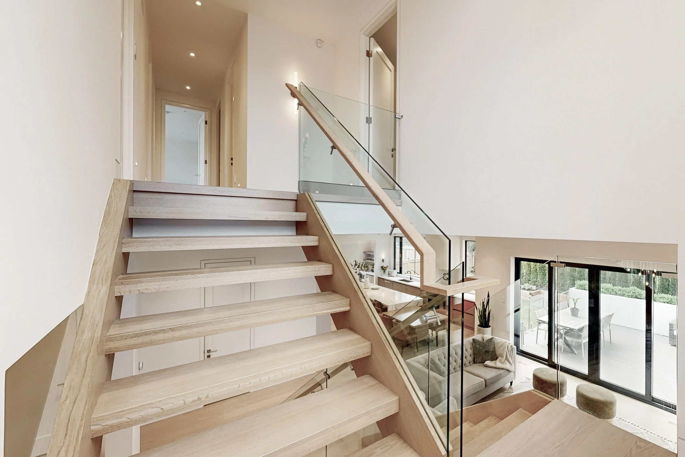 Mid-landing view down the open oak staircase with glass railings overlooking the main floor.
