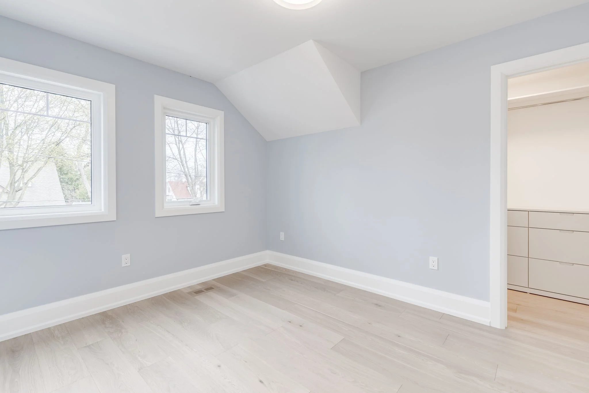 Bright upper-floor bedroom with a sloped dormer ceiling, light oak flooring, and a walk-in closet in a completed second storey addition.