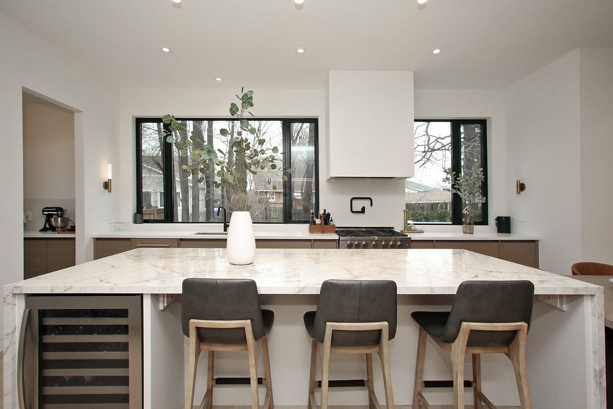 A finished Waterfront kitchen in Etobicoke: a black-and-white modern kitchen with a large marble waterfall island, grey leather stools, black-framed windows, and a pro range under a plaster hood.