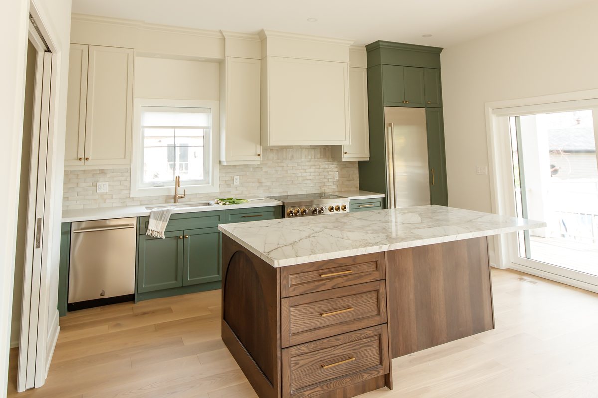 A finished Waterfront kitchen in Etobicoke: sage-green base cabinets and cream uppers around a marble-topped walnut island, with a tiled backsplash, a gas range, and glass doors to the garden.